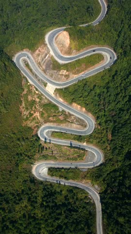 Aerial view of winding mountain road in Ha Giang, Vietnam. Sharp curves, lush green forest, and dramatic terrain create stunning aerial view of scenic Asian landscapes and travel routes.