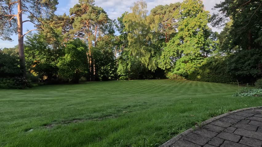Well-maintained garden with trimmed green lawn, patterned mowing lines, trees in the background, and stone paved path, tranquil outdoor park landscape ideal for relaxation, nature, and design.