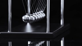 Newton's cradle pendulum with steel balls in motion, demonstrating physics principles of momentum and energy transfer in dramatic lighting - Powered by Shutterstock - Get 15% off with code: PIKWIZARD15
