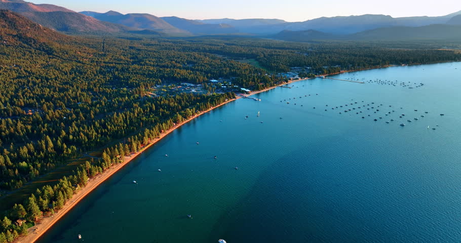 Lake Tahoe waterscape with wooded lakefront. Drone footage at the shore. Multiple boats stand on the water.