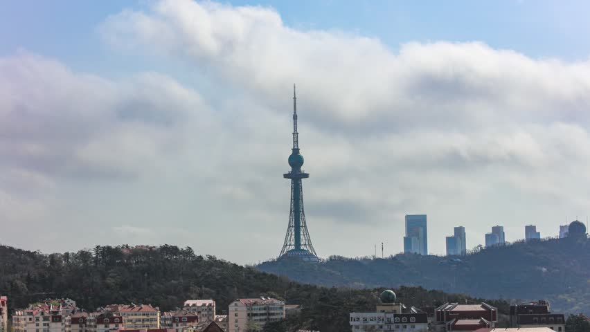 Time lapse of towering TV transmission tower and streaming clouds over Qingdao cityscape with residential buildings and urban skyline against dramatic sky