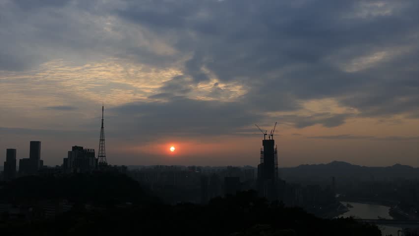 Dramatic sunset over Chongqing urban skyline with construction cranes and communication tower silhouetted against golden sky, showcasing China