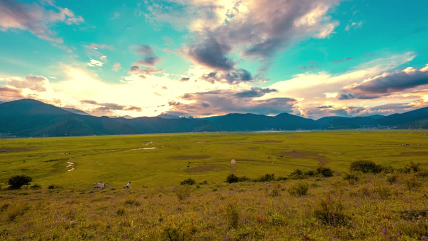 Stunning time lapse view of Shangri La Yila grassland with dramatic sunset clouds over mountain landscape in Yunnan, China. Golden hour natural beauty.