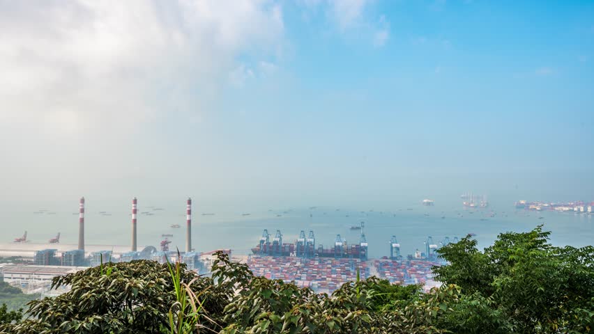 Aerial view of Chiwan Ferry Terminal and Shenzhen port with industrial smokestacks, shipping containers, and cargo cranes along the waterfront under blue sky