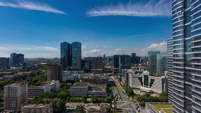 Aerial view of modern Shenzhen cityscape with skyscrapers, urban development, and green spaces under blue sky with white clouds in China