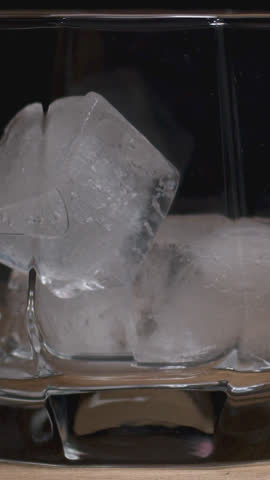 Glass of whiskey on a wooden table with chocolates and sticks on a dark background. Crystals bakal with an alcoholic drink. 4K.