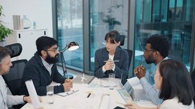 Diverse team of young professionals sitting around table discussing wind power project. Multiracial group planning renewable energy strategy in bright modern office with blue glass walls. Indoors. - Powered by Shutterstock - Get 15% off with code: PIKWIZARD15