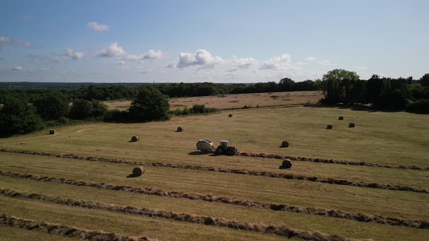 Tractor harvesting grass and making hay bales in field, aerial drone view. Aerial drone footage of a tractor working in an agricultural field during summer. The machine harvests grass and packs it 
