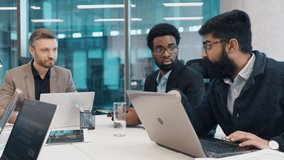 Three male professionals collaborating during business meeting at office table, one explaining data on laptop. Team focused on digital strategy, charts and tech devices visible around. - Powered by Shutterstock - Get 15% off with code: PIKWIZARD15