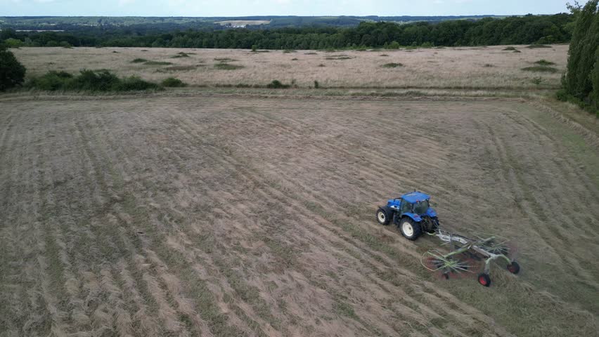 Tractor harvesting grass and making hay bales in field, aerial drone view. Aerial drone footage of a tractor working in an agricultural field during summer. The machine harvests grass and packs it 