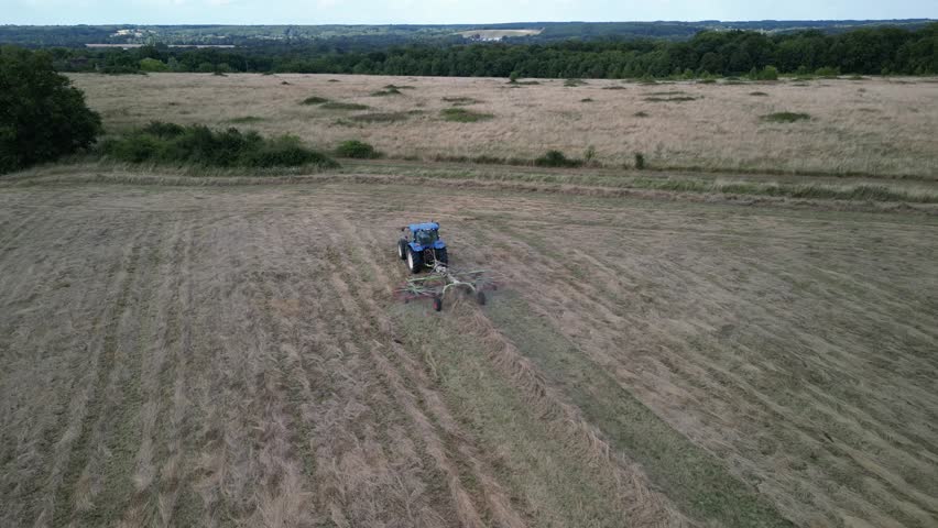 Tractor harvesting grass and making hay bales in field, aerial drone view. Aerial drone footage of a tractor working in an agricultural field during summer. The machine harvests grass and packs it 