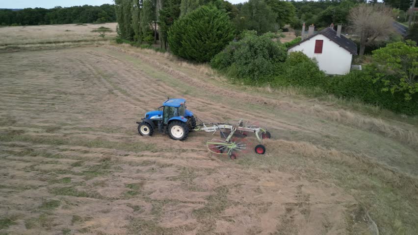 Tractor harvesting grass and making hay bales in field, aerial drone view. Aerial drone footage of a tractor working in an agricultural field during summer. The machine harvests grass and packs it 