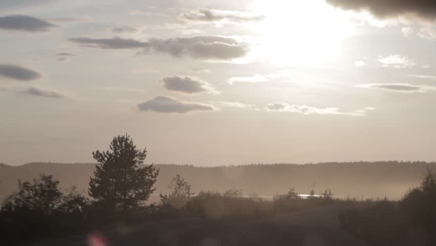 A stunningly beautiful sunset scene showcasing calm, reflective waters, silhouetted trees, and soft, dreamy clouds