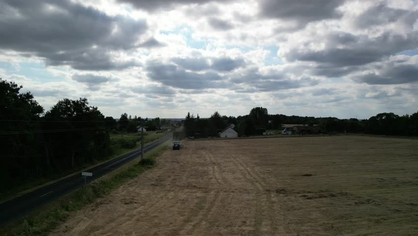 Tractor harvesting grass and making hay bales in field, aerial drone view. Aerial drone footage of a tractor working in an agricultural field during summer. The machine harvests grass and packs it 