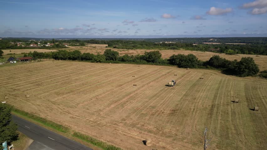 Tractor harvesting grass and making hay bales in field, aerial drone view. Aerial drone footage of a tractor working in an agricultural field during summer. The machine harvests grass and packs it 