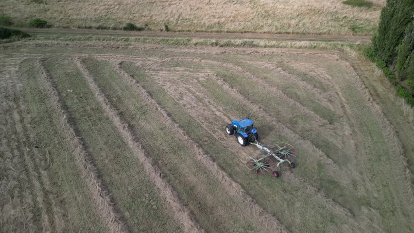 Tractor harvesting grass and making hay bales in field, aerial drone view. Aerial drone footage of a tractor working in an agricultural field during summer. The machine harvests grass and packs it 