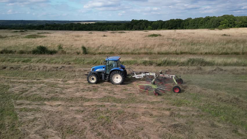 Tractor harvesting grass and making hay bales in field, aerial drone view. Aerial drone footage of a tractor working in an agricultural field during summer. The machine harvests grass and packs it 