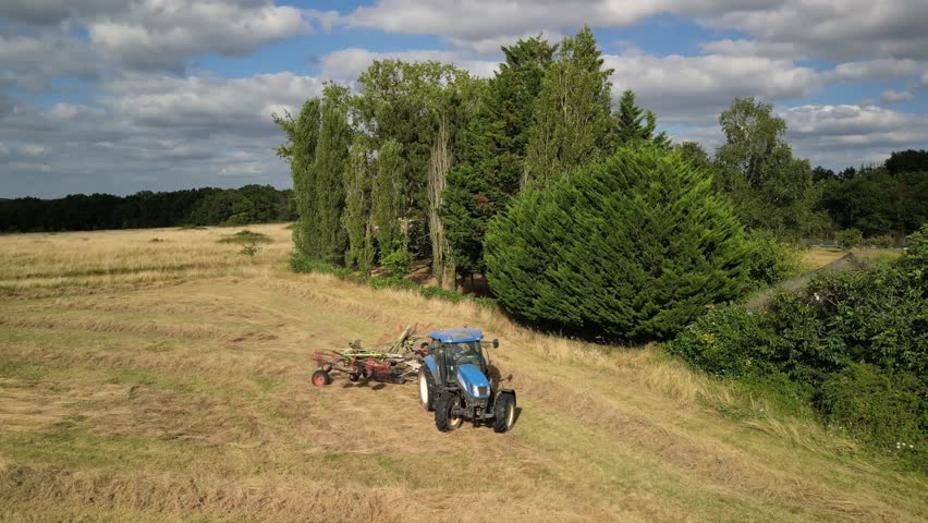 Tractor harvesting grass and making hay bales in field, aerial drone view. Aerial drone footage of a tractor working in an agricultural field during summer. The machine harvests grass and packs it 