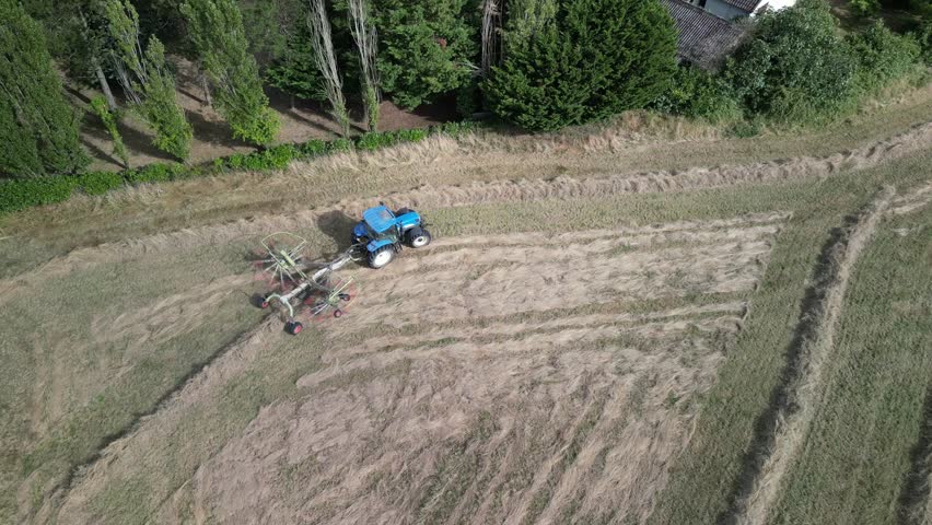 Tractor harvesting grass and making hay bales in field, aerial drone view. Aerial drone footage of a tractor working in an agricultural field during summer. The machine harvests grass and packs it 