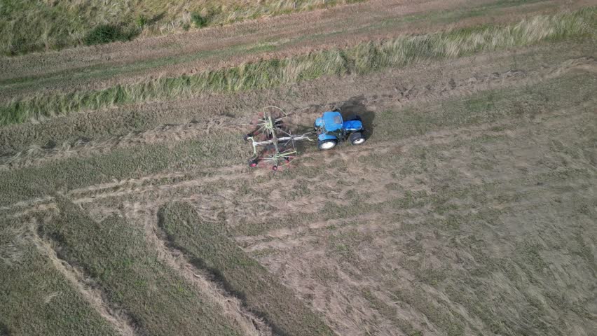 Tractor harvesting grass and making hay bales in field, aerial drone view. Aerial drone footage of a tractor working in an agricultural field during summer. The machine harvests grass and packs it 