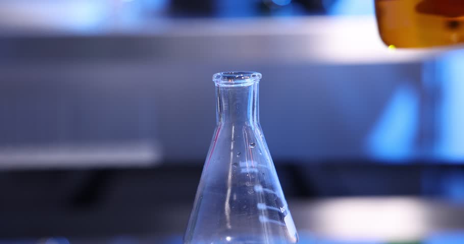 Woman pouring orange liquid from glass beaker into flask in laboratory, closeup