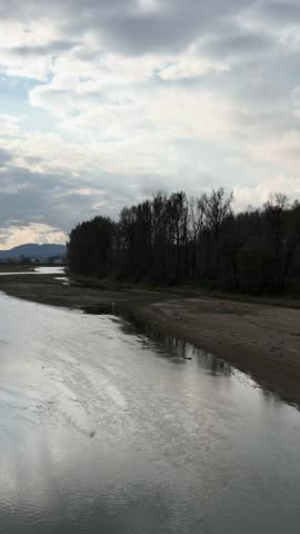 Serene River Landscape in British Columbia, Canada with Reflective Water and Dark Treeline Under Cloudy Sky