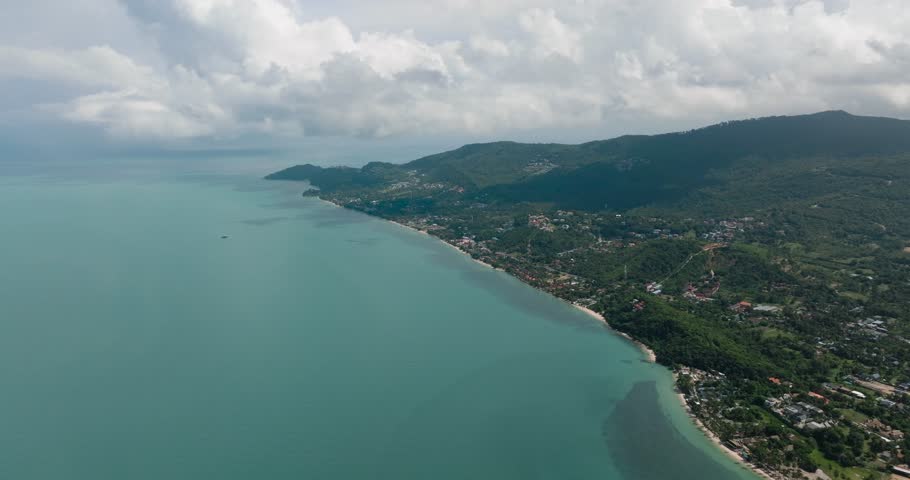 Turquoise sea and lush green hills along a serene coastline under blue skies. Ko Samui, Thailand.
