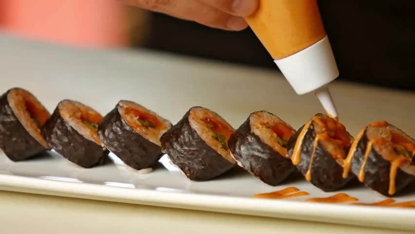Close-up of sushi rolls with spicy sauce topping, served on a white plate. Japanese fusion food in 4K.