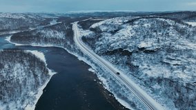 Murmansk, Russia - December 13, 2024: Aerial view of a black Jetour T2 SUV driving on a snowy road situated between a partially frozen river and a steep, snow-dusted, rocky hill in the arctic valley - Powered by Shutterstock - Get 15% off with code: PIKWIZARD15