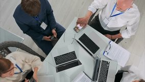 Top view of a group of business professionals using smartphones during a meeting in a modern office. Several laptops, documents, and ID badges are visible on the table. Digital communication. - Powered by Shutterstock - Get 15% off with code: PIKWIZARD15