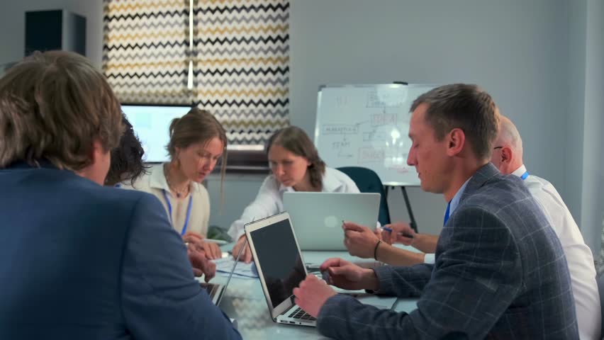 Concentrated group of young professionals reviewing financial statistics, using laptops and printed charts during an office meeting. Team members collaborate and discuss data in a modern workspace. - Powered by Shutterstock - Get 15% off with code: PIKWIZARD15