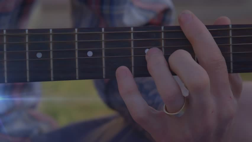 Left hand pressing chords then sliding finger for next chord change in sunny outdoor music tutorial. Music, craftsmanship, acoustic, rustic, harmonious, lifestyle, performance