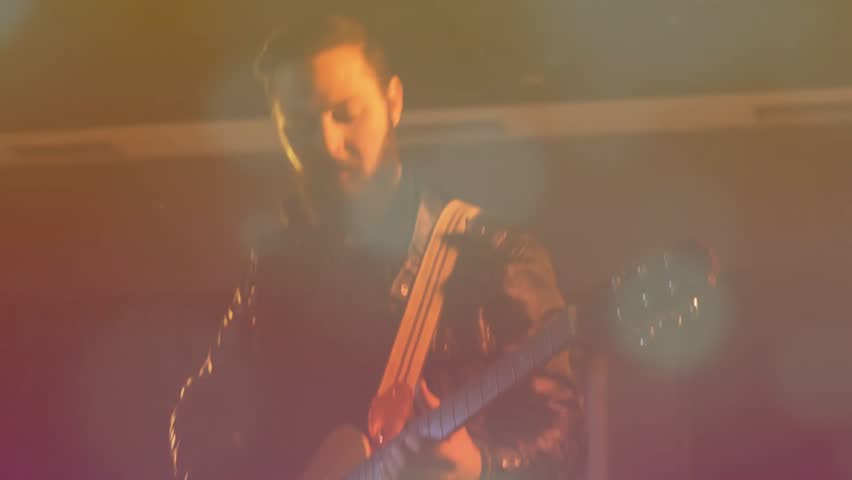 Bearded guitarist strumming guitar under lights sparking bassist, singer harmonizing for music show. Rock band, live concert, stage performance, musical act, vibrant lighting, instrumental ensemble,