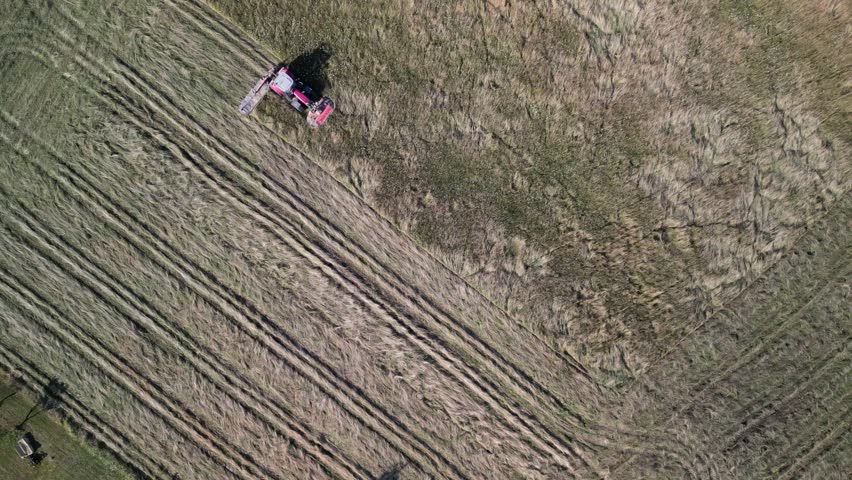 Tractor harvesting grass and making hay bales in field, aerial drone view. Aerial drone footage of a tractor working in an agricultural field during summer. The machine harvests grass and packs it