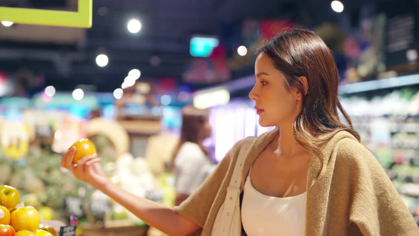 Happy beautiful Asian woman choosing and buy fresh fruit and vegetable with using reusable mesh cotton shopping bag at shopping mall supermarket. Sustainable living and healthy lifestyle concept.
