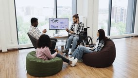 Diverse professionals discussing financial report in office. Includes young wheelchair user leading conversation and mixed gender team interacting around monitor with graphs. - Powered by Shutterstock - Get 15% off with code: PIKWIZARD15