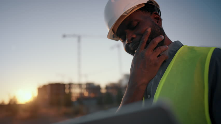 Problems at construction site, foreman looking at laptop display and thinking. Medium portrait of thoughtful builder or architect with computer, examining plant and drawing, engineer making decision