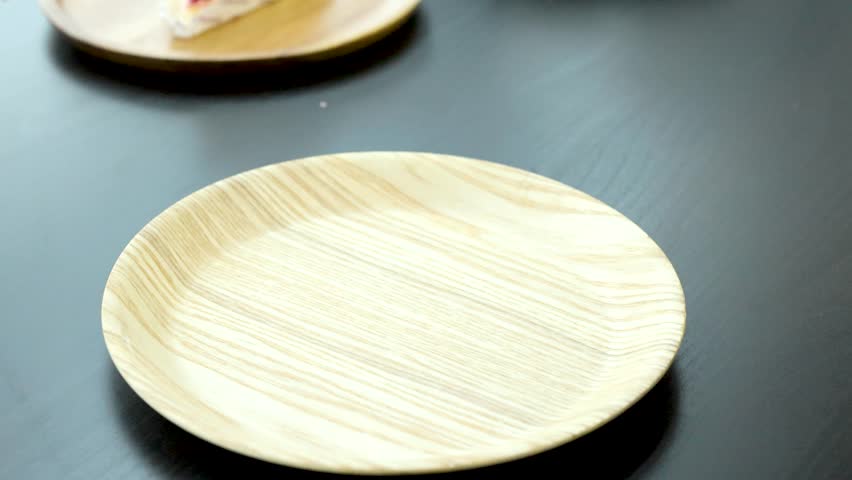 Hand places chocolate cake slice with strawberry topping onto round wooden plate, bright natural lighting