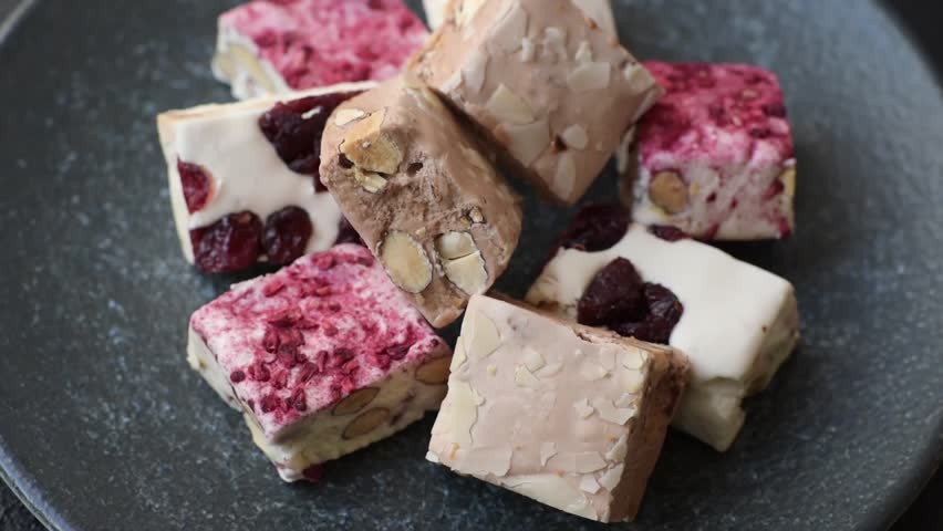 Nougat or white caramel with hazelnuts and pistachios and strawberry pieces. White nougat with nuts, sweets for the festive table