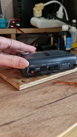 Upper angle shot of a female hand with a ring operating a black vintage cassette recorder, pressing the red record button on a warm wooden tabletop.