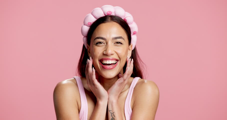 Face, beauty and woman in studio with wink, healthy skin and cosmetology in self care. Smile, confidence and female person with headband on pink background, wellness and treatment in skincare routine