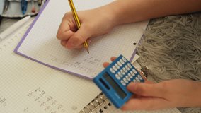 Close-up of young student's hands diligently writing in notebook, solving mathematical equations with pencil and using small calculator for assistance with school homework - Powered by Shutterstock - Get 15% off with code: PIKWIZARD15
