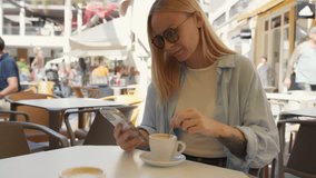 Beautiful woman with glasses sit at street cafe terrace, stirring coffee while browsing social media on mobile phone and enjoy sunny day during vacation break.Travel, tourism, food and drink. - Powered by Shutterstock - Get 15% off with code: PIKWIZARD15