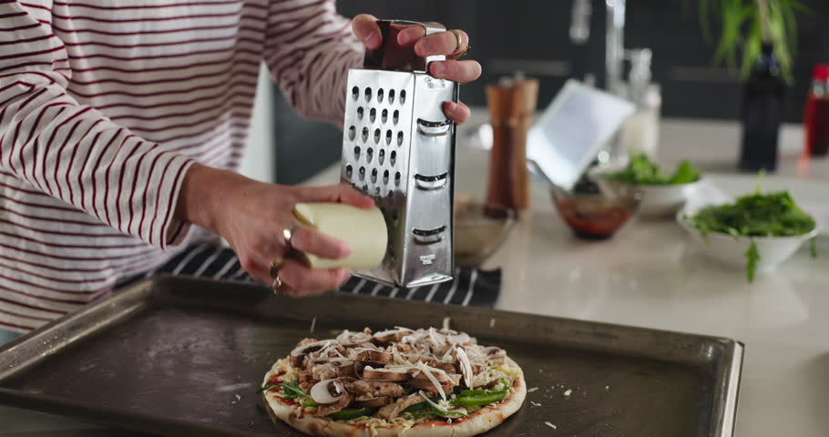 Person, hands and cheese with grater for pizza, food or lunch snack on oven tray in kitchen. Culinary, chef or ingredients with flavor or meal prep for italian cuisine or parmesan recipe in home