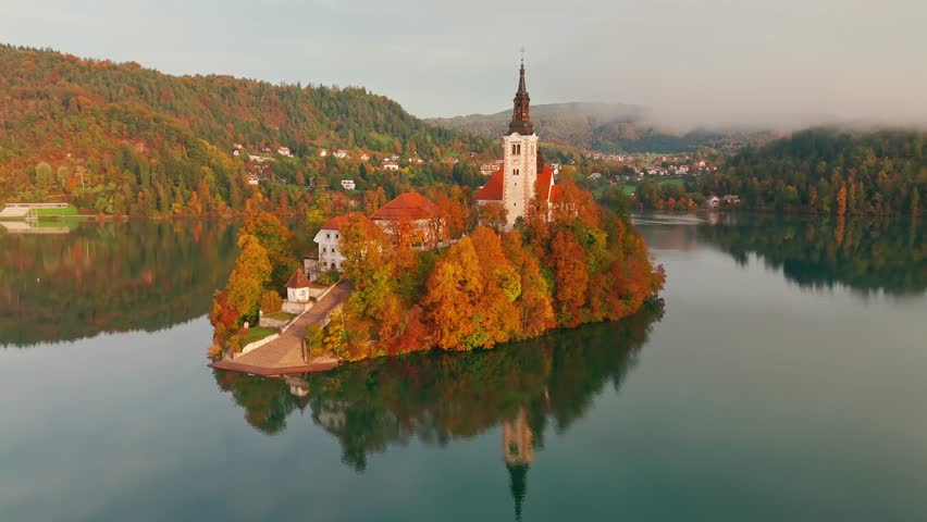 Aerial view of Lake Bled at sunrise in autumn, Slovenia. Scenic landscape with Pilgrimage Church on the island and medieval Bled Castle on a cliff above the picturesque lake surrounded by mountains.