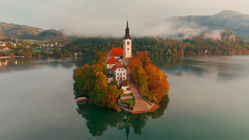 Aerial view of Lake Bled at sunrise in autumn, Slovenia. Scenic landscape with Pilgrimage Church on the island and medieval Bled Castle on a cliff above the picturesque lake surrounded by mountains.