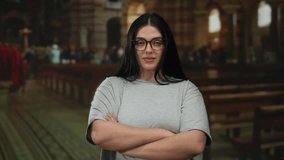 Young woman with glasses standing confidently in a church, wearing casual attire and expressing empowerment through her pose in an indoor religious setting. - Powered by Shutterstock - Get 15% off with code: PIKWIZARD15