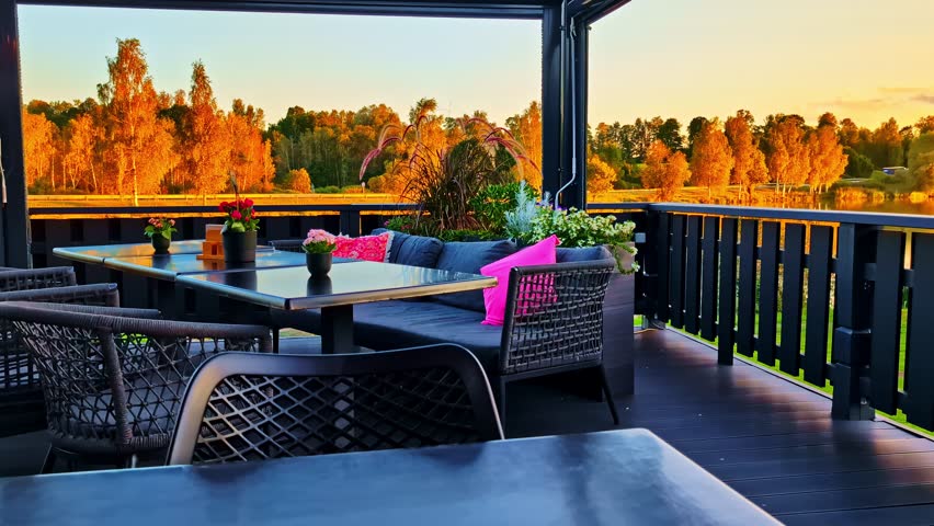 Cozy Restaurant Patio Lounge with Flower Pots Overlooking Forest Lake During Golden Sunset at Autumn with Colorful Trees