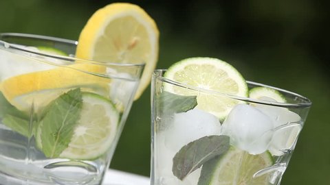 Glass with ice cubes, mint, lemon and lime and jug with pouring lemonade. स्टॉक व्हिडिओ