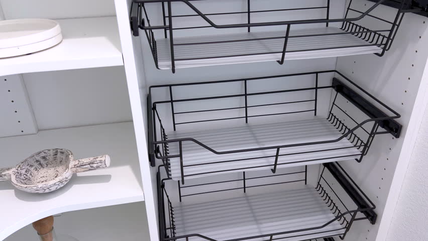 Close interior view of a pantry with white shelving and several black wire pull out baskets. The design emphasizes functional and organized modern kitchen storage.